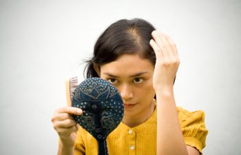 Woman suffering from hair loss watching her scalp in a mirror.
