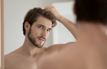 A handsome man looking at his hair in a mirror.