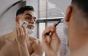 Man shaving face in front of the bathroom mirror.