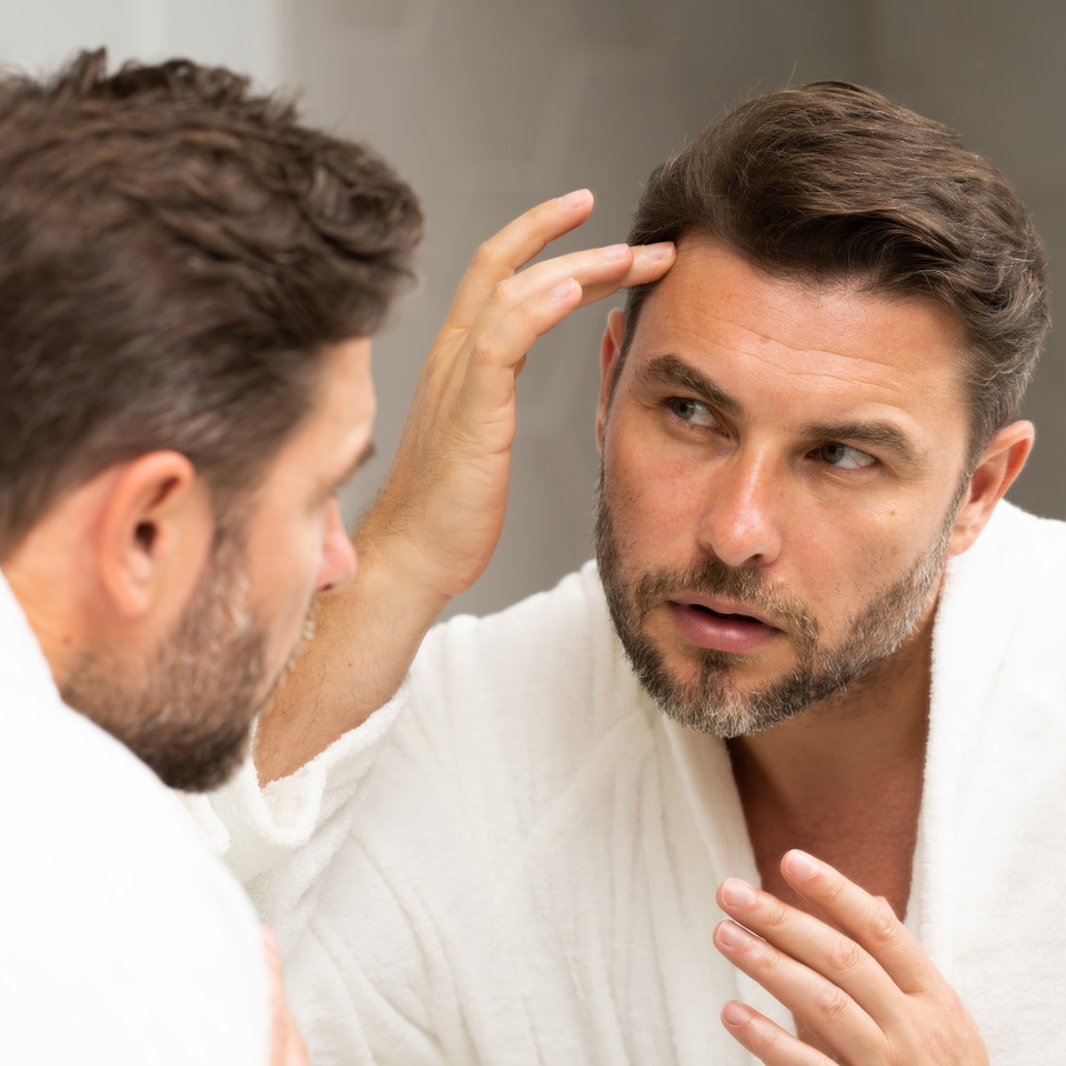 a man in a bathrobe in the bathroom looking at his wrinkles and pimples on his face. A man is looking at his reflection in a mirror. A man is looking at his reflection in a mirror.