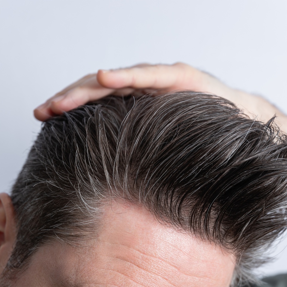 Close-up of an unrecognizable man combing his toupee with his hand. Styling and hair care concept