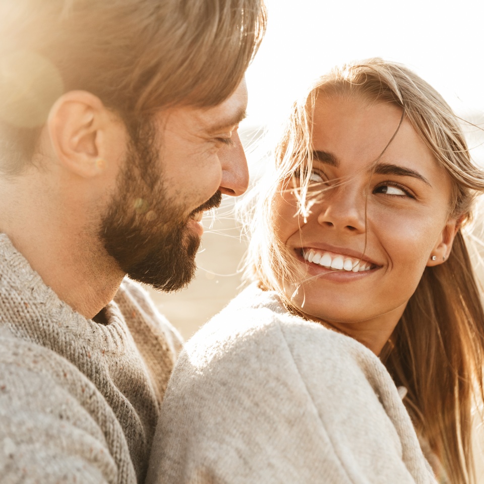 Close up of a smiling beautiful young couple embracing while standing at the beach