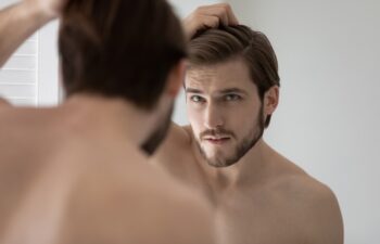 Anxious young Caucasian man look in mirror in bathroom touch check head worried about dandruff, concerned millennial male frustrated about hair loss, receding hairline, haircare, beauty concept